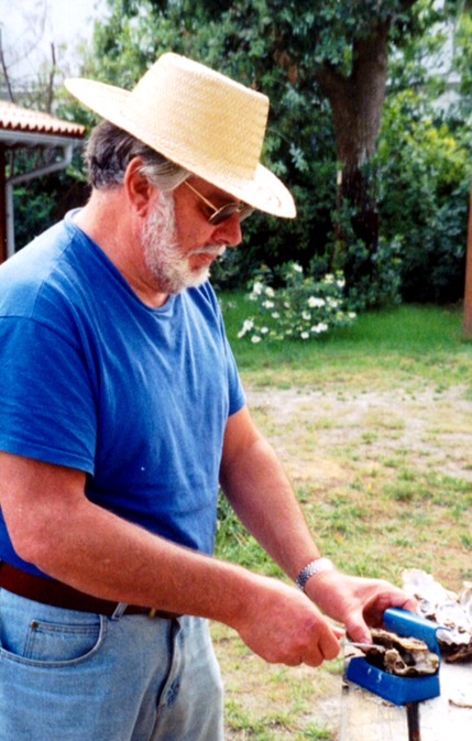 A man in a straw hat opening oysters outdoors