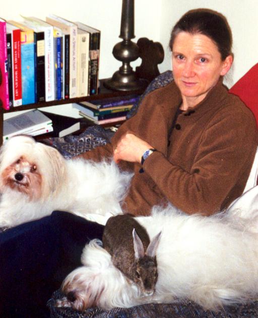 A woman seated by bookshelves with a white dog and a cat
