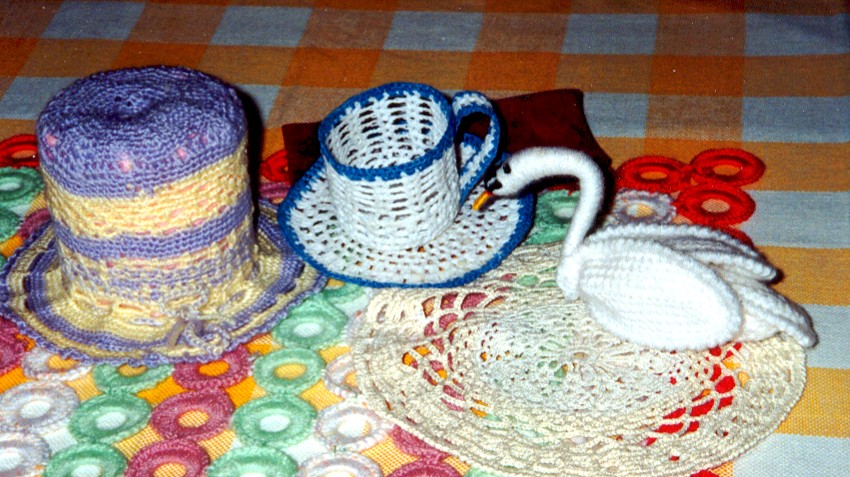 Crocheted pieces including a swan and a teapot on a colorful cloth