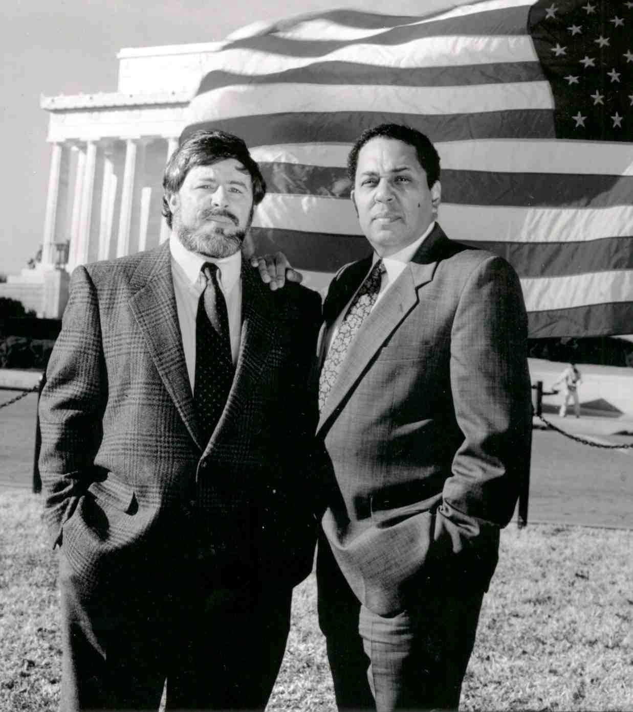 Two men in suits in front of an American flag