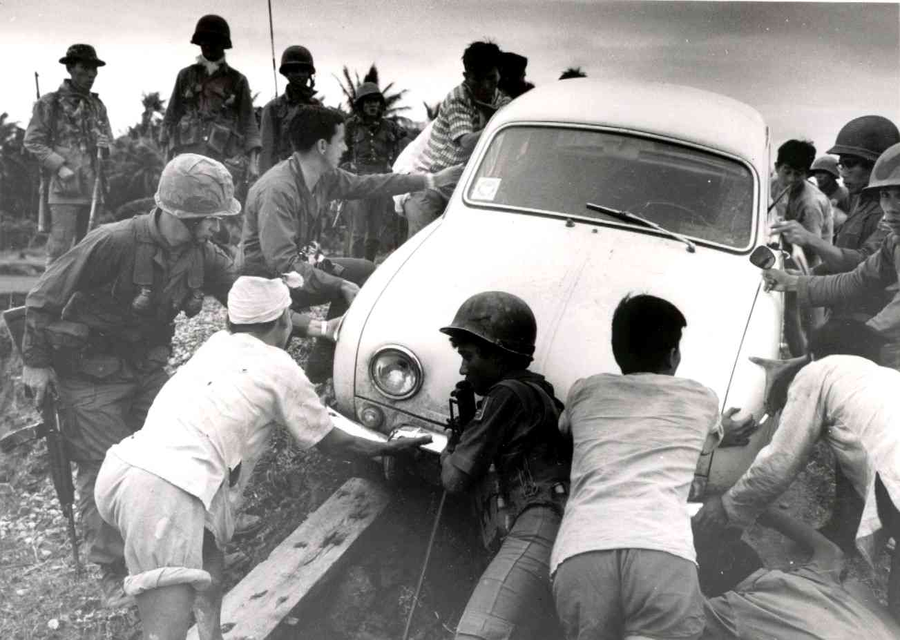 Soldiers pushing a car on a dirt road