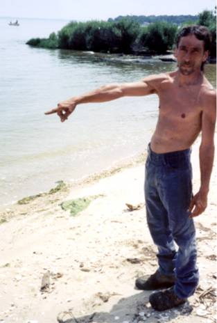 A man on a beach pointing across the water